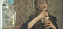 a woman is drinking from a glass in front of a fridge .
