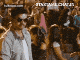 a man wearing sunglasses stands in front of a crowd of people with the website starttamilchat.in in the corner