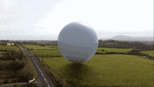 a large white ball is floating over a grassy field