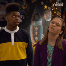 a boy and a girl are standing in front of a wall with a picture of a rocket on it