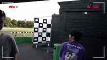 a man in a purple surf 's up shirt stands in front of a checkered board