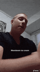 a man in a black shirt is eating moonbeam ice cream from a container