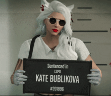 a woman is holding a sign that says " sentenced in lspd kate bublikova # 201896 "