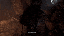 a man with a beard is standing in a cave holding a sword and talking to another man .