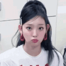 a close up of a girl wearing a white shirt and red earrings .