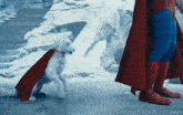a dog wearing a red cape is standing next to a man in a superman costume