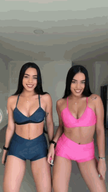 two women standing next to each other wearing bikinis and shorts