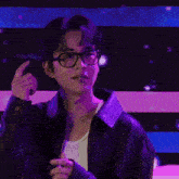 a man wearing glasses and a leather jacket holds his hand out
