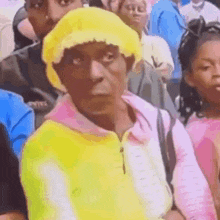a woman wearing a yellow hat and a pink sweater is sitting in a crowd of people .