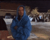 a man wearing a blue hoodie is standing in a parking lot