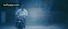 a man is riding a motorcycle down a dark street in the rain .