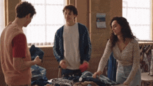 a group of people standing around a pile of clothes with a calendar on the wall