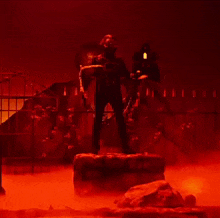 a man wearing a mask and a black jacket is standing in front of a red wall .