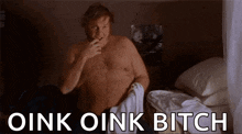 a shirtless man is sitting on a bed smoking a cigarette and the words oink oink bitch are above him .