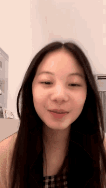 a woman with long black hair is smiling in front of a white wall