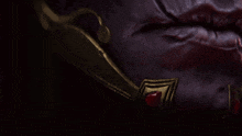 a close up of a purple and gold item with a red stone on it
