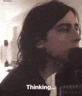 a man with long hair is singing into a microphone and the word thinking is on the bottom of the screen