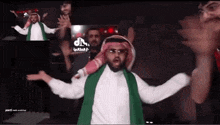 a man in a white shirt and a green scarf is standing in front of a sign that says tiktok