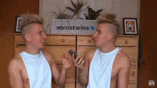 two shirtsless men are standing in front of a sign that says vorostwins