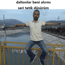 a man is sitting on a railing with his arms outstretched in front of a river .