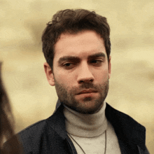a man with a beard is wearing a turtleneck sweater and a jacket