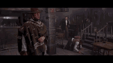 a man wearing a poncho is standing next to a man laying on the floor .