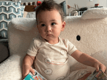 a baby is sitting on a couch holding a book that says ' avengers ' on it