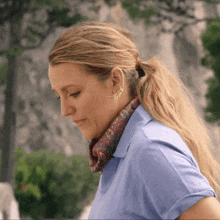 a woman in a blue shirt with a scarf around her neck looks down