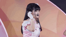 a girl wearing a pink dress and white gloves is talking into a microphone