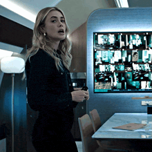 a woman in a black shirt stands in front of a wall with a lot of images on it