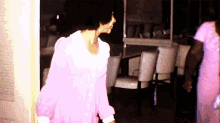a woman in a pink dress is walking in a room with chairs