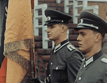 two men in military uniforms are standing in front of a flag