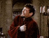 a man in a red robe is laughing with his hands on his hips