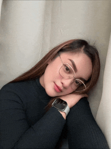 a woman wearing glasses and a smart watch rests her head on her hand