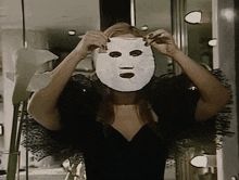a woman in a black dress is putting on a white mask
