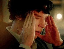 a man in a suit is holding his head with both hands .
