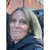 a woman in a black jacket is making a funny face in front of a crosswalk sign .