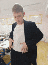 a boy in a suit and white shirt is standing in a classroom