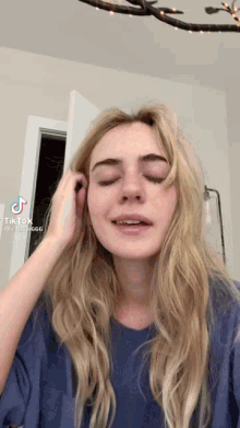 a woman with long blonde hair is wearing a blue shirt and covering her ears .