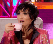 a woman in a pink sequined jacket is drinking from a cup
