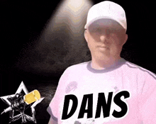 a man wearing a pink shirt and a white hat is standing in front of a microphone with the word dans on it .