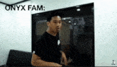 a man in a black shirt is standing in a room with the words onyx fam written above him .