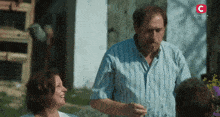 a man in a blue striped shirt stands next to a woman in a white shirt with a red c on the bottom right