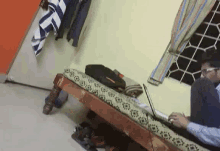 a man is sitting on a bed using a laptop .