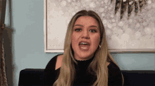 a woman is sitting on a couch with her mouth open in front of a painting that says ' christmas ' on it