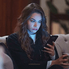 a woman is sitting on a couch and looking at her phone .