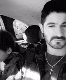 a man with a beard and a cross necklace is sitting in a car with two children