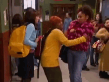 a woman in a yellow sweater is hugging another woman in a red hat in a hallway .