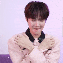 a young man wearing a pink sweater is covering his mouth with his hand