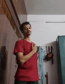 a man in a red shirt is standing in a room with his hands on his chest